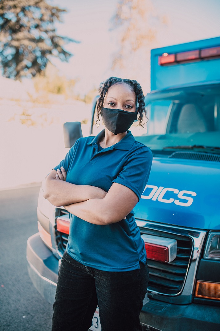 Female paramedic standing in front of an ambulance wearing a mask